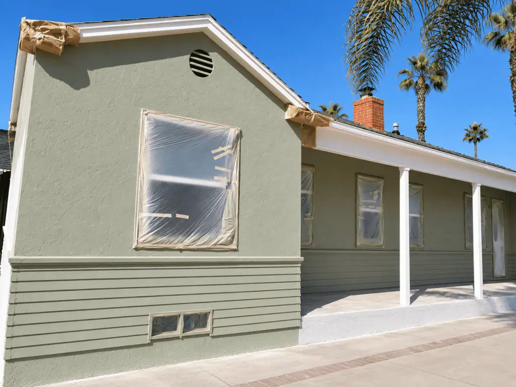 Exterior view of a renovated house with fresh green paint and new windows.